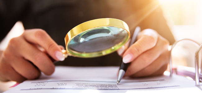 human hand holding magnifying glass over invoice